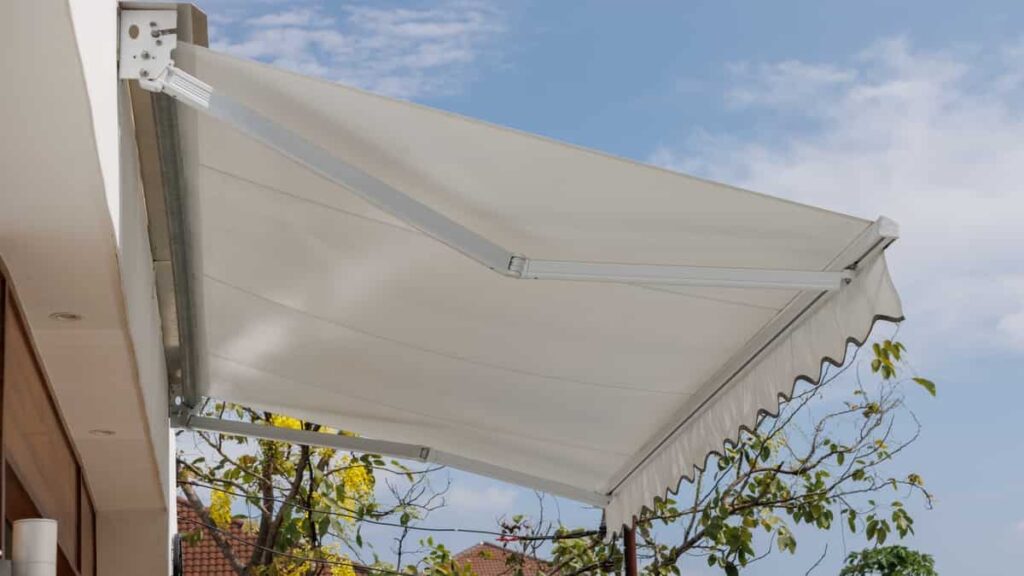 Terrasoverkapping met een witte doek en een tafel met stoelen.
