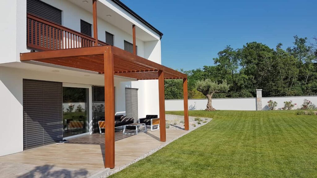 Een houten terrasoverkapping in een grote tuin.