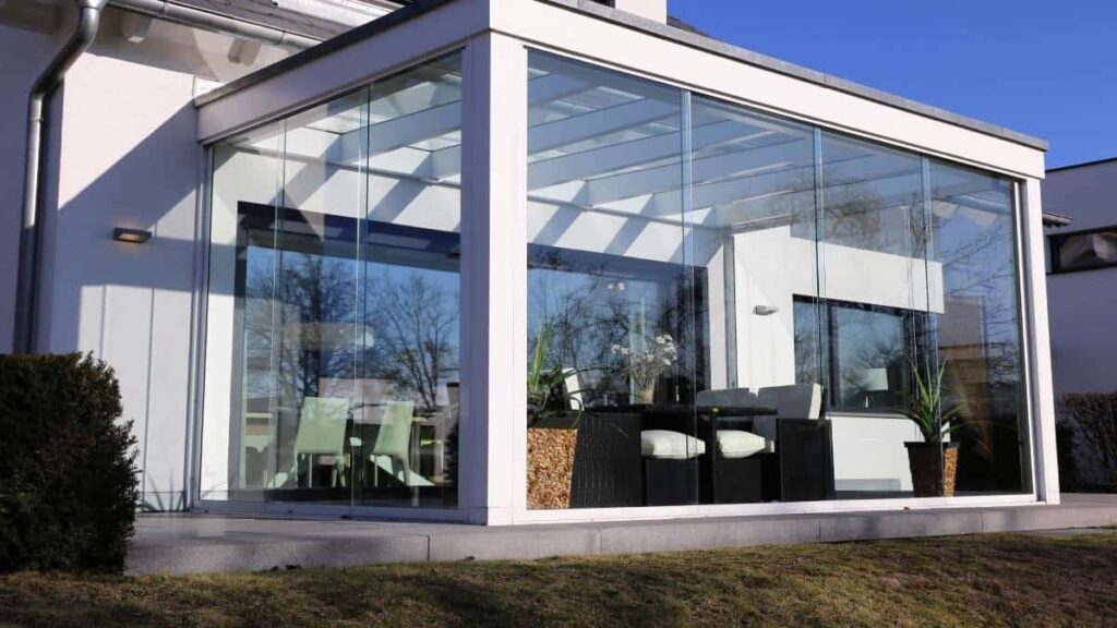 Een gesloten, witte veranda met grote raampartijen.